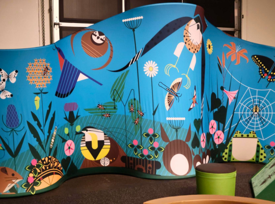 A blue panel with drawings of birds and flowers from "i am wild: a charley harper exhibit."