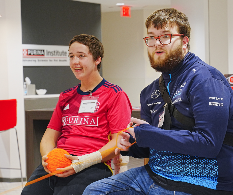 Two students laugh while holding parts of a large yarn web.