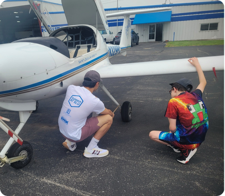 2025-camp-report-aviation A student looks at the wheel of a small plane with an instructor.
