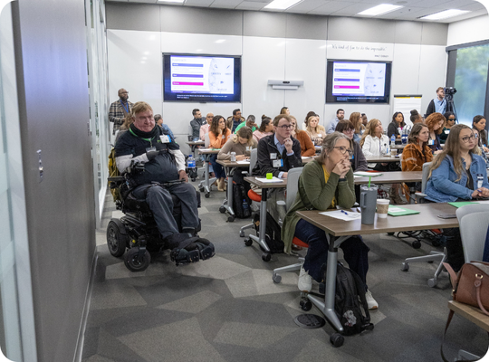 A large conference room filled with attendees listening to a presenter.