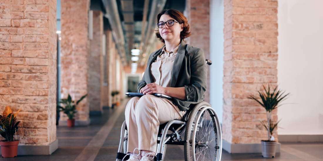 Professional who uses a manual wheelchair smiling in an office setting.