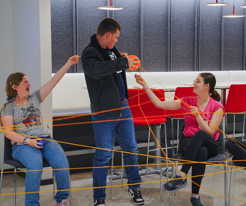 Yarn game at Purina Three students laugh while holding parts of a large yarn web.