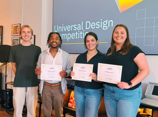 College students, 3 holding certificates, smile together in an office with screen behind them.